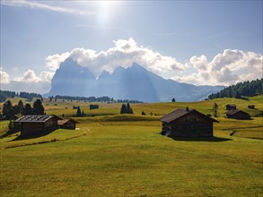 Alpine huts on autumn-coloured pastures in front of Sassolungo and Sassopiatto with clouds, Alpe di