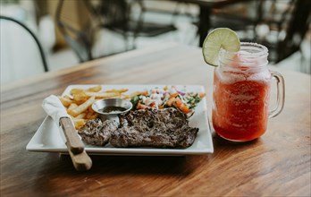 Nicaraguan skirt steak with fries and drink served on wooden table. Delicious homemade steak with