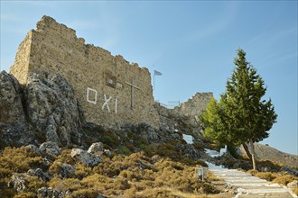 Stone ruin with cross on a hill, stairway and Greek flag under a clear sky, St John's Castle, Oxi