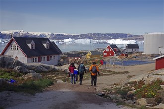 Three people walk through a village of colourful houses towards a shore lined with icebergs,