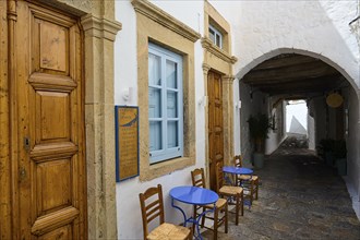 Small coffee tables with blue chairs in front of a building with wooden doors and arches in a