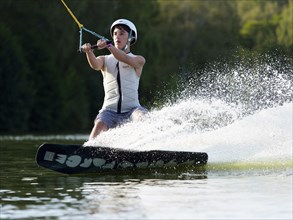 Sporty young man with helmet and waistcoat on wakeboard in lake, water sports, water skiing in