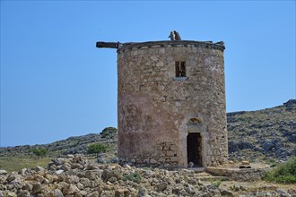 Abandoned old mill on a hill, surrounded by stones, under a clear blue sky, windmill, ruin, near