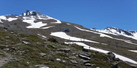 Snow-covered mountain with cable car supports and ski slopes under a blue sky, Pico del Veleta,