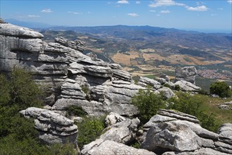 Huge rock formations in front of a wide landscape with fields and mountain ranges under a clear