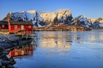 Typical Norwegian red house, fjord with ice floes in front of steep mountains, reflection, morning