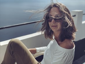 Woman with sunglasses smiles relaxed with wind in her hair by the sea