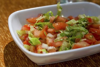 Close-up of a fresh salad with tomatoes, onions and green leaves in a white ceramic bowl on a