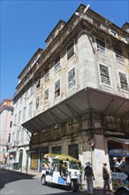 Dilapidated historic building with a tuk-tuk on a street under a clear blue sky, Rua Nova do