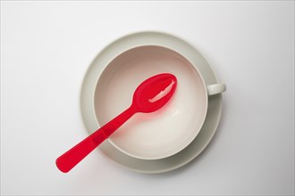 Crockery and cutlery, empty teacup with saucer, seen from above, a red plastic spoon lies on it