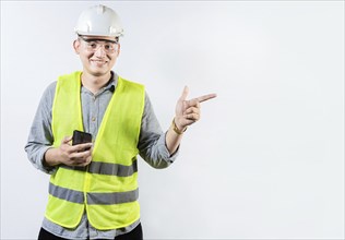 Smiling engineer holding cell phone and pointing an advertisement. Young latin engineer holding