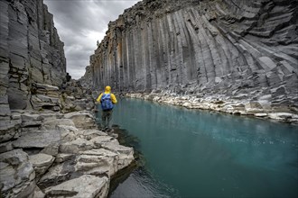 Tourist standing by the river in Stuðlagil Canyon, turquoise blue river between basalt columns,