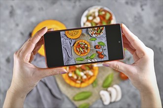 Taking photo of food with hands holding mobile phone with picture of vegan baked Red kuri squash