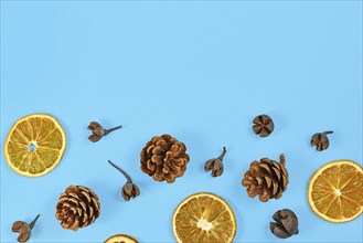 Seasonal autumn flat lay with dried orange slices and fir cones on blue background with empty copy