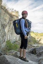 Portrait of female climber looking at camera at foot of rocky mountain. Extreme outdoor sport