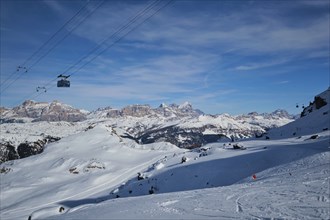 View of a ski resort piste with people skiing in Dolomites in Italy with cable car ski lift. Ski