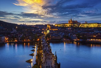 Aerial view of illuminated Prague castle and Charles Bridge with tourist crowd over Vltava river in