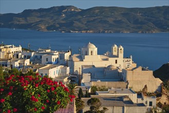 View of Plaka village on Milos island over red geranium flowers on sunset. Plaka town, Milos