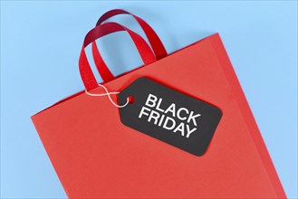 Black Friday sale label on red paper shopping bag on blue background