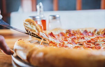 Homemade ham and cheese pizza with spatula on table. Hand taking a slice of ham pizza with the