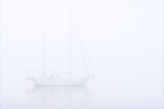 Sailboat, sailing boat, yacht with lowered sails anchored at sea during bad visibility due to thick