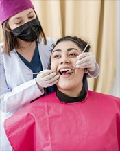 Dentist checking patient with excavator and dental mirror, Front view of dentist checking patient