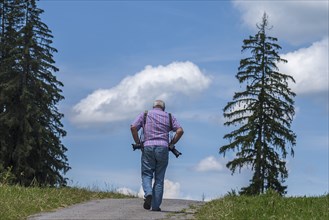 Photographer with equipment looking for motifs in the mountains, Eisenberg (Ostallgäu), Bavaria,