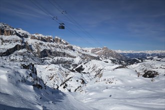 View of a ski resort piste with people skiing in Dolomites in Italy with cable car ski lift. Ski