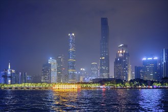 Guangzhou cityscape skyline over the Pearl River with tourist boat illuminated in the evening.