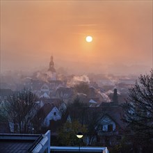 View of the town from above, houses and church tower in autumn, sunrise in the fog, smoky chimneys,