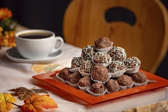 A plate of rum balls on a table with autumnal decorations and a cup of coffee