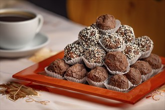 Close-up of rum balls with chocolate on a plate and a coffee cup in the background