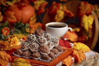 Autumnally decorated table with rum balls, colourful leaves and a cup of coffee in a cosy