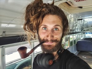 Close up portrait shot of a curious looking young man with long hair, big headphones and a wooden