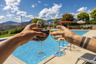 Young caucasian happy couple enjoying spiritual alcoholic drinks on swimming pool, hand holding red