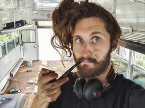 Close up portrait shot of a funny looking young man with long hair, big headphones and a wooden