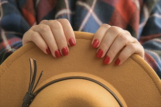 Stylish red female nails. Woman in poncho holding brown trendy hat. Modern Beautiful manicure.