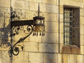 Old wrought iron lamp and window with security bars on the stark wall of the Convent of San Paio de