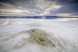 Wide closed ice field of a lake under a cloudy sky with distant horizon, camping site, Hegne, Lake