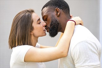 Side view close-up of a tender multi-ethnic couple with white clothes kissing and embracing