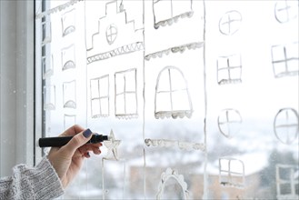 Female hand draws christmas holidays decoration painted on window glass. New Years scenery. city