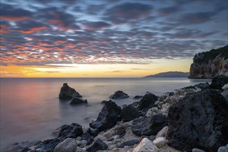 A colorful sunrise at Cala Gonone with black and white rocks and boulders in the foreground