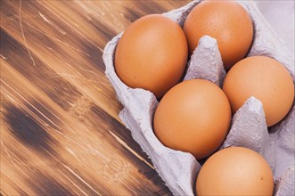 Image shows some raw eggs in a box on a wooden plate