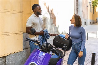 Multi-ethnic couple talking beside a scooter motorbike parked in the street