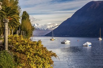 Sheltered sailboats in lake lugano, view from park Helenium with columns and snow-capped mountains