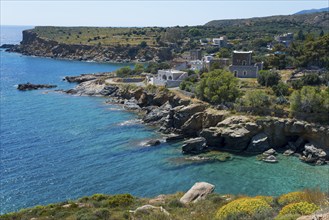 Coastal landscape with rocky shores, clear blue water and picturesque houses under a clear sky,