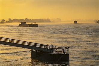 Cargo ships on the Rhine near Emmerich, early morning, sunrise, fog, mist on the river, jetty in