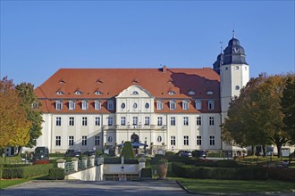 Large castle with a red roof against a blue sky, surrounded by autumn trees, Malchower See,