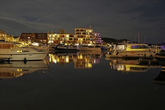 Marina at night with illuminated buildings and reflection in the water, Waren, Müritz,