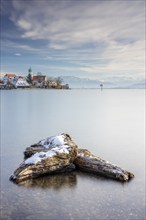 Wooden trunks picturesque church of St. George on the lakeshore in front of snow-covered Pfänder on